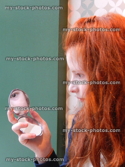 Stock image of girl looking at herself in compact mirror