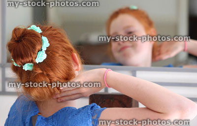 Stock image of girl with red hair in bun, looking in mirror, posing