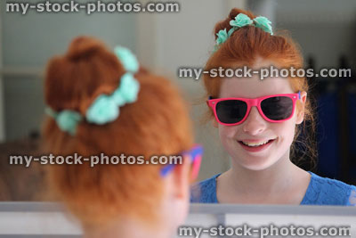 Stock image of girl with red hair in bun, looking in mirror, sunglasses