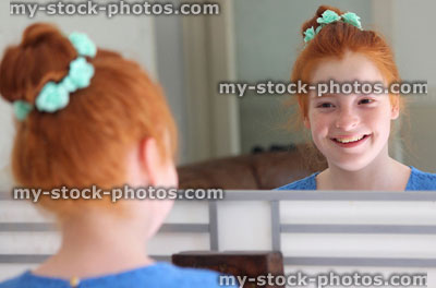 Stock image of girl with red hair in bun, looking in mirror, posing