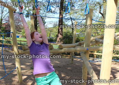 Stock image of young girl playing in woodland playground, hanging on monkey bars