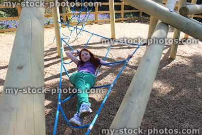 Stock image of young child playing in woodland playground, wooden climbing frame net