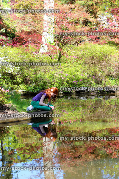 Stock image of girl sitting by pond looking at water, fish and reflection