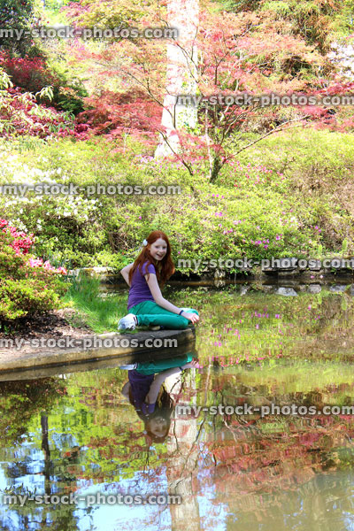 Stock image of girl sitting by pond looking at koi carp fish swimming