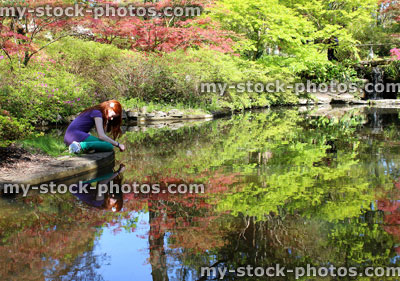 Stock image of girl sitting by pond looking at goldfish swimming and reflection