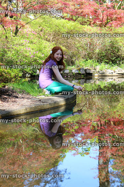 Stock image of girl sitting by pond looking at water, fish and reflection