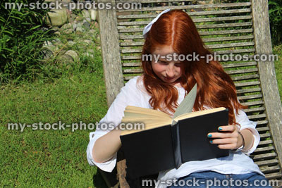 Stock image of girl reading book in garden, wooden steamer / sunlounger