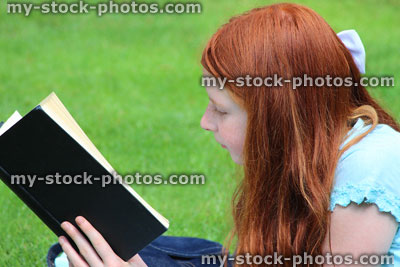 Stock image of young girl reading school book on garden lawn