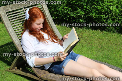 Stock image of young girl reading book, wooden garden sunlounger / steamer