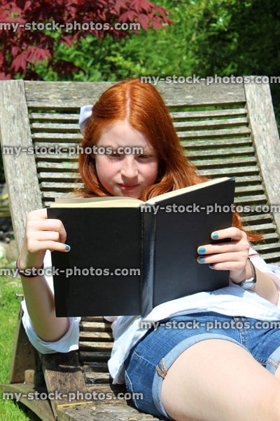 Stock image of young girl reading book, wooden garden sunlounger / steamer