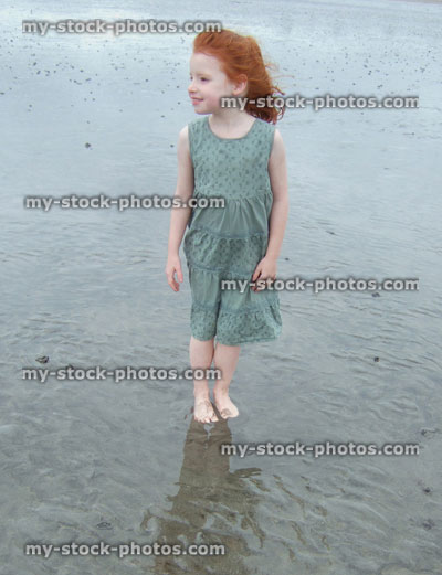 Stock image of little girl standing on wet sandy beach, reflections