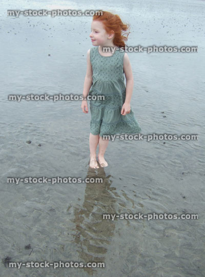 Stock image of little girl standing on wet sandy beach, reflections