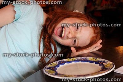 Stock image of girl sat at restaurant table pulling funny face, waiting for food