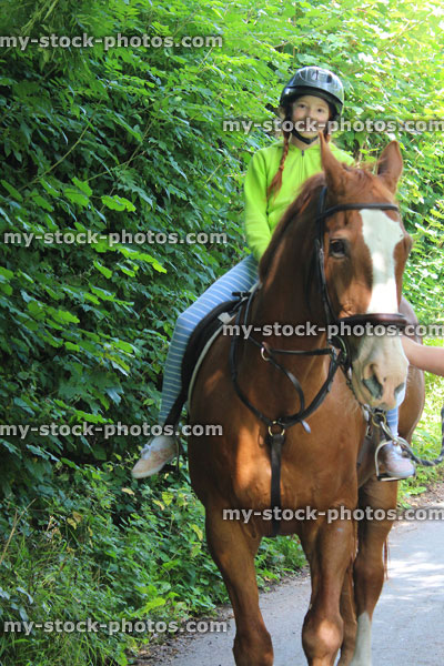 Stock image of young girl enjoying horse riding lesson, wearing equestrian helmet hat