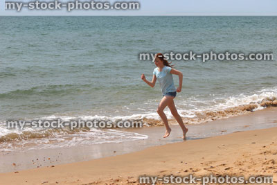 Stock image of girl running barefoot on beach by sea / seaside exercise