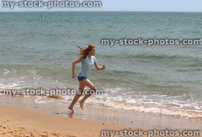 Stock image of girl running barefoot on beach by sea / seaside exercise