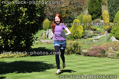 Stock image of red haired girl running across sunny garden lawn