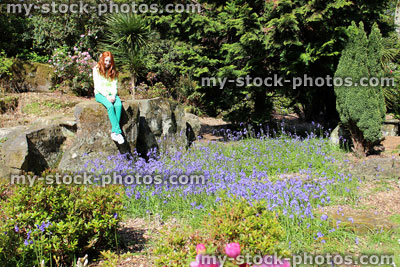 Stock image of girl sitting in rock garden (rockery) with flowers and conifers