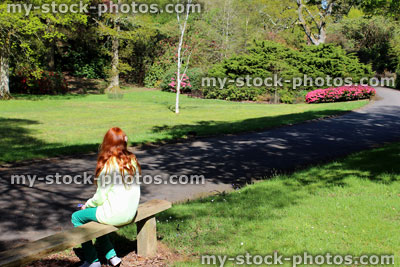 Stock image of girl with long red hair sat on sunny garden bench