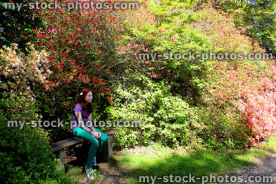 Stock image of girl sat on wooden garden bench by azalea / rhododendron flowers