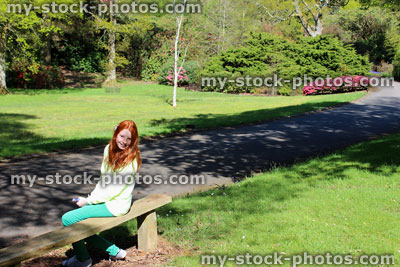 Stock image of girl with long red hair sat on sunny garden bench