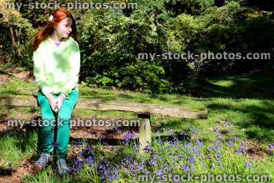 Stock image of girl sat of rustic wooden garden bench with woodland bluebells