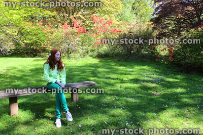 Stock image of girl sitting on rustic wooden bench, garden lawn in shade
