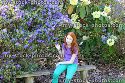 Stock image of girl sat on wooden bench by rhododendron flowers