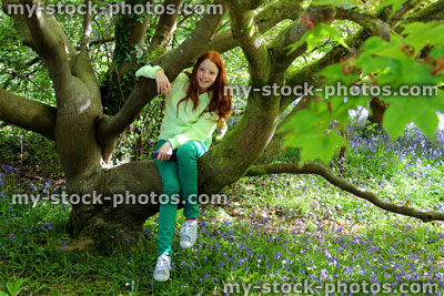 Stock image of red head girl climbing on trunk and branches of rhododendron tree