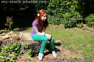 Stock image of young girl with long red hair sitting on tree trunk