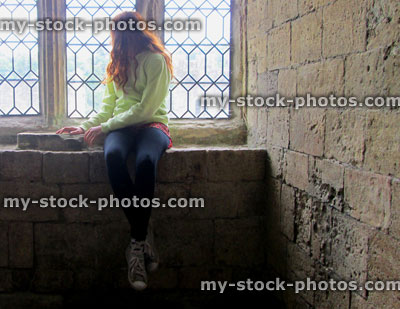 Stock image of girl sat on windowsill by wall, looking out leaded window