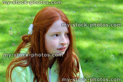 Stock image of girl with long red hair looking puzzled on garden lawn