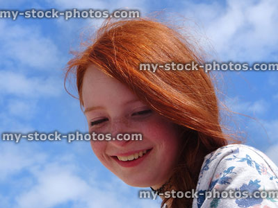 Stock image of pretty smiling girl with red hair against blue sky