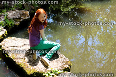 Stock image of girl sitting on stepping stones across pond in Japanese garden
