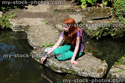 Stock image of girl sitting on stepping stones across pond in Japanese garden