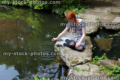 Stock image of girl sitting on stepping stones across pond in ornamental garden