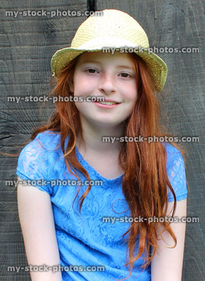 Stock image of girl sitting in garden, wooden background, long red hair, hat, blue dress