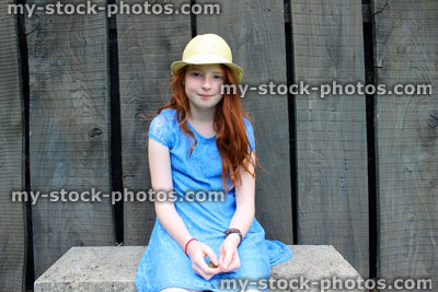 Stock image of girl sitting on garden bench with long hair, hat, dress