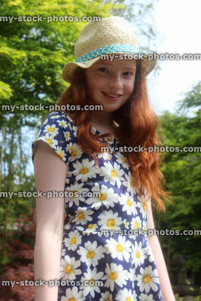Stock image of happy girl in summer garden, wearing straw hat in sunshine
