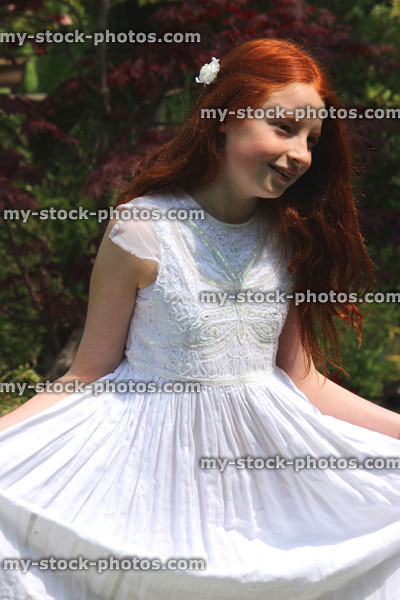 Stock image of happy girl in garden, wearing long flowing white summer dress