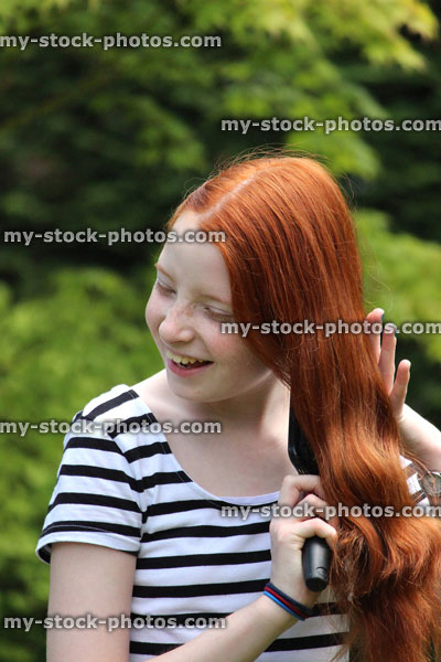 Stock image of attractive girl brushing her long red hair outside in sunshine
