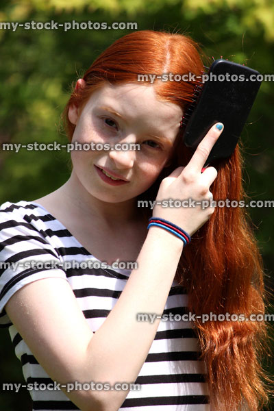 Stock image of beautiful girl brushing her long red hair outside in sunshine