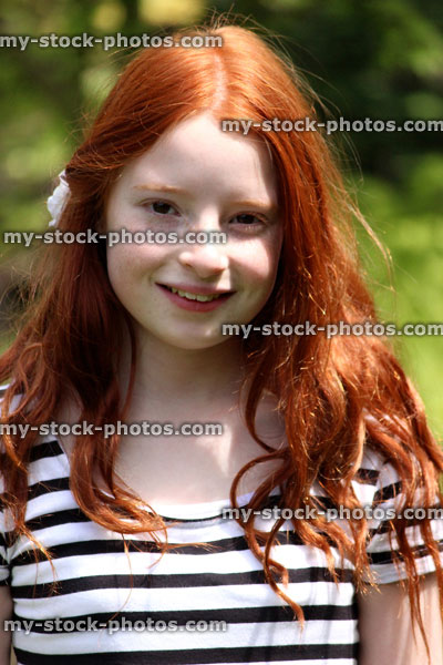 Stock image of pretty, happy girl with long red hair, pictured smiling to herself in the sunshine outside