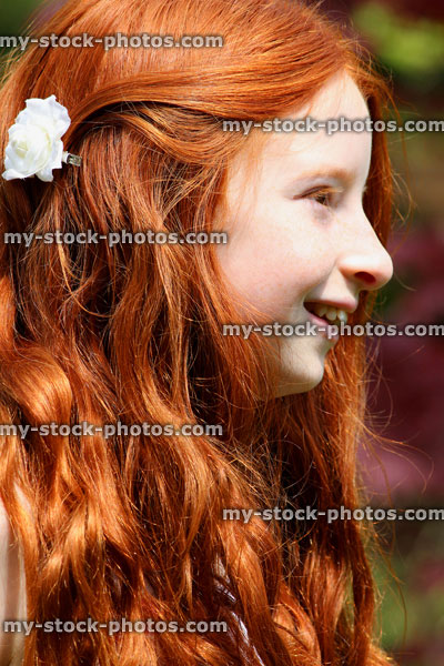 Stock image of pretty, happy girl with long red hair, pictured smiling to herself in the sunshine outside