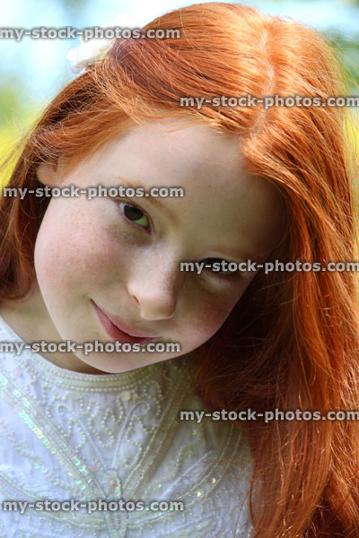 Stock image of pretty, happy girl with long red hair, pictured smiling to herself