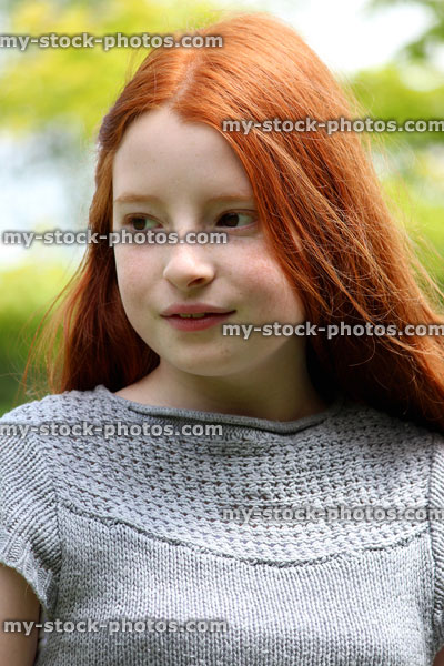 Stock image of pretty, happy girl with long red hair, pictured on a sunny day outside