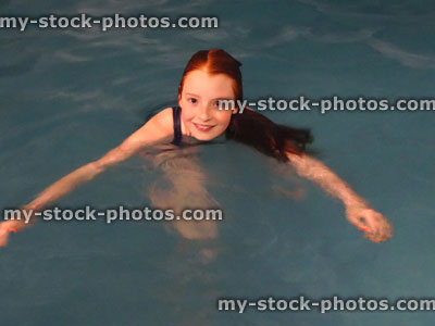 Stock image of young girl playing in blue swimming pool, floating