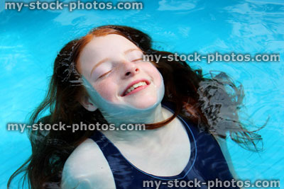 Stock image of young girl playing in blue paddling pool, submerged
