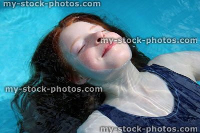 Stock image of young girl playing in blue paddling pool, floating