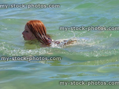 Stock image of girl with red hair, swimming in sea water